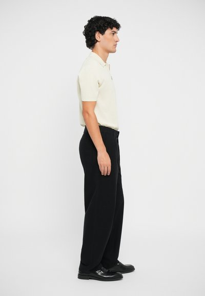 Camisa polo en beige claro, de manga corta. Combinada con pantalones negros de pierna ancha y zapatos negros. Líneas limpias, diseño minimalista.