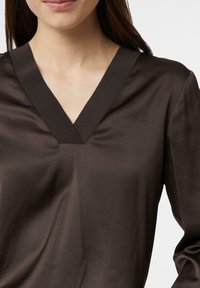 Braune V-Ausschnitt-Bluse mit langen Ärmeln, aus glattem Stoff gefertigt. Verfügt über ein schlichtes Design und minimale Nähte.