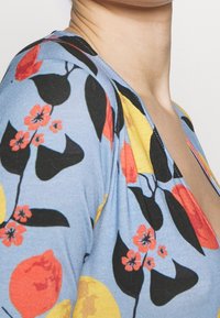 Mehrfarbige Bluse mit einem blauen Hintergrund und floralen Mustern in Rot, Schwarz und Gelb. Weicher Stoff mit einem tiefen V-Ausschnitt.