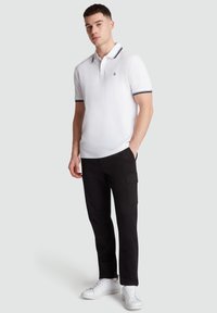 Witte polo met een marineblauwe gestreepte kraag, gecombineerd met zwarte cargo broek en witte sneakers. Eenvoudige, relaxte pasvorm met korte mouwen.