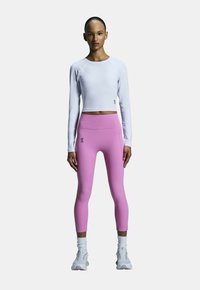 Weißes kurzärmeliges Oberteil mit langen Ärmeln und rosa hochtaillierte Leggings. Mit Logo-Details und weichem, dehnbarem Stoff. Die Schuhe sind graue Sport Schuhe.