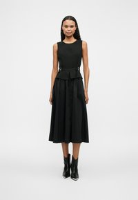 Μαύρο φόρεμα με εφαρμοστό κορσέ, ζώνη peplum με ασημί λεπτομέρειες και φαρδιά φούστα. Συνδυάζεται με μαύρες μποτές μέχρι τον αστράγαλο. Λείος υφή.