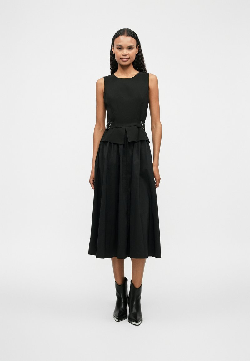 Μαύρο φόρεμα με εφαρμοστό κορσέ, ζώνη peplum με ασημί λεπτομέρειες και φαρδιά φούστα. Συνδυάζεται με μαύρες μποτές μέχρι τον αστράγαλο. Λείος υφή.