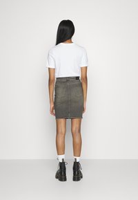 Falda de mezclilla gris con dobladillo deshilachado, de cintura alta y dos bolsillos traseros, combinada con una camiseta blanca y botas negras con cordones.