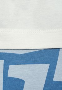 Light blue cotton T-shirt featuring a contrasting textured white hem and a bold blue graphic design across the lower section.