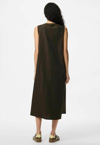 Vestido marrón sin mangas con corte recto, dobladillo a la altura de la rodilla y textura suave, combinado con zapatillas casuales. Se muestra la vista trasera.