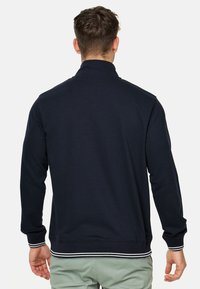 Tamnoplavi zip-up dukserica s visokim ovratnikom, rebrastim manžetama i rubom s bijelim prugama. Izrađena od mekog materijala, idealna za ležerno nošenje.
