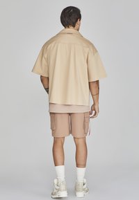 Maglietta beige a maniche corte con una vestibilità comoda, abbinata a pantaloni cargo light brown con tasche e sneakers beige con calze bianche.