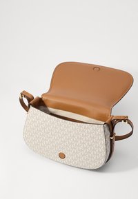 Sac à bandoulière en cuir beige avec un devant en tissu crème à motif. Il dispose d'une fermeture à pression magnétique et d'un intérieur ouvert pour un accès facile.