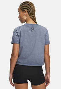 Camiseta azul corta hecha de tejido suave, con manga corta y un logo gráfico en la parte posterior. Combinada con pantalones cortos negros.