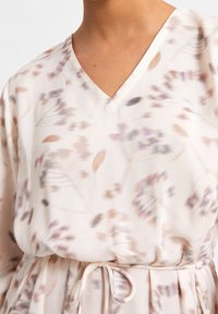 Vestido de flores con escote en V en tejido ligero, que presenta colores suaves pastel, una cintura con lazo y un patrón fluido y texturizado con hojas y pétalos.