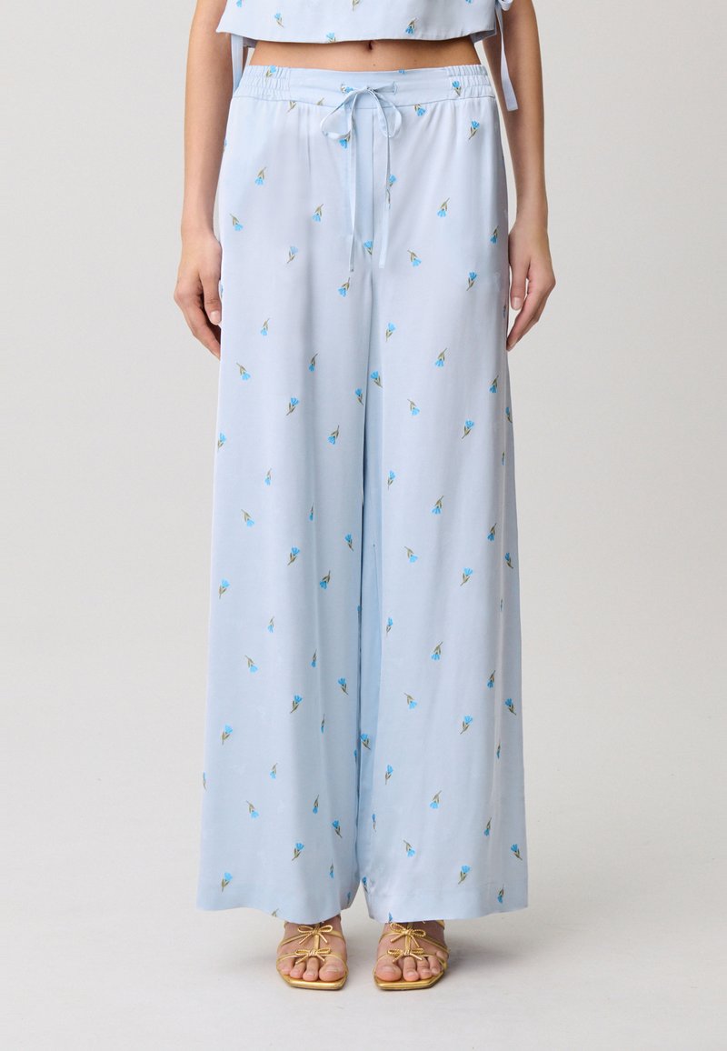 Pantaloni a gamba larga azzurri in tessuto liscio, con piccoli motivi floreali in blu e verde, dotati di elastico in vita e coulisse.