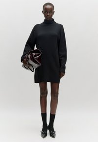 Schwarzes, übergroßes Rollkragenkleid mit langen Ärmeln, kombiniert mit schwarzen Socken und schmalen, patentierten Leder-Pumps. Dunkelrote Clutch.
