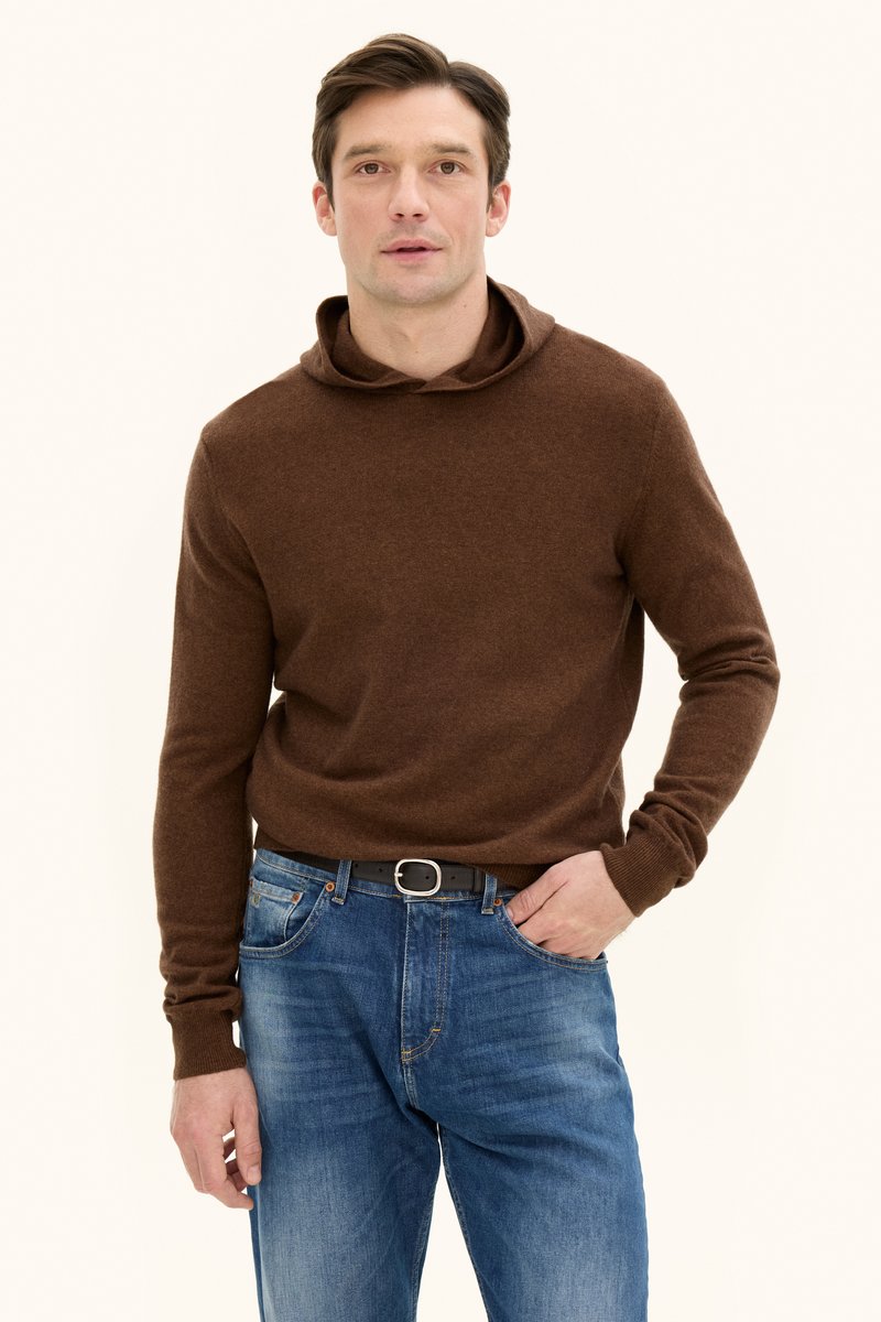 Brauner Pullover mit Kapuze, aus strukturiertem Stoff. Kombiniert mit blauen Jeans, die einen schwarzen Gürtel mit einer silbernen Schnalle haben. Schlichtes Design.