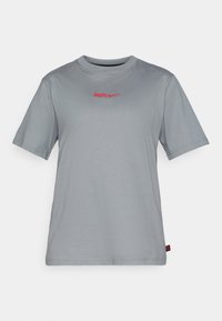 Jasnoszara koszulka typu t-shirt z krótkim rękawem, okrągłym dekoltem, z czerwoną napisem "ATLET" oraz logo w formie łyżwy z przodu. Miękka, gładka tekstura tkaniny.