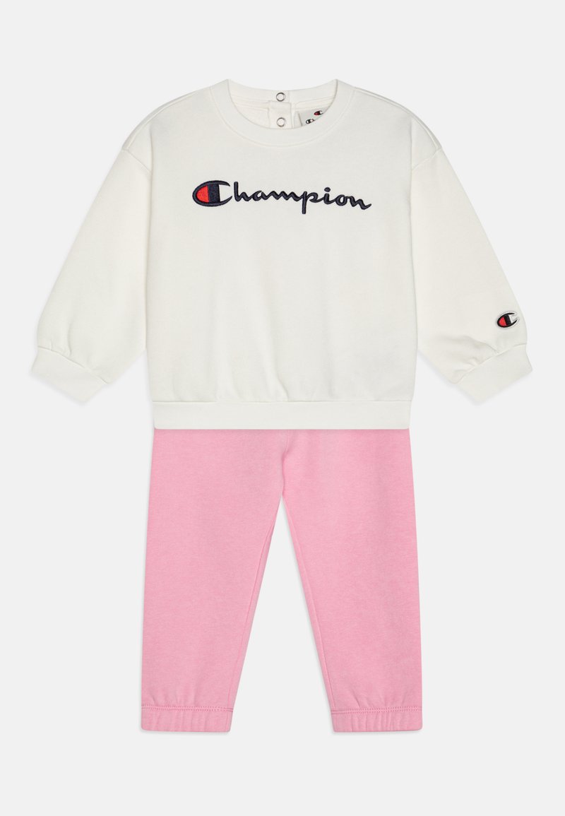 Sudadera blanca con el logo "Champion" en azul marino y rojo; pantalones rosa con puños elásticos; tejido suave; conjunto de dos piezas casual.