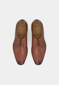 Chaussures en cuir marron à texture lisse, bout pointu et quatre œillets pour les lacets. Logo estampillé à l'intérieur, fabriquées en Italie.