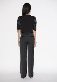 Schwarzes Oberteil mit glänzenden Puffärmeln, kombiniert mit maßgeschneiderten schwarzen Hosen. Glatte Textur, taillierte Passform und subtile Akzente an den Hosen.