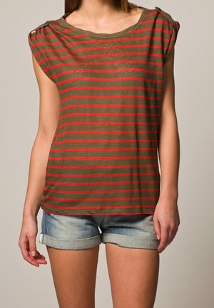 Olivengrøn kortærmet top med røde striber, der har en rund halsudskæring og skulderdetaljer. Sammen med lyse denimshorts.