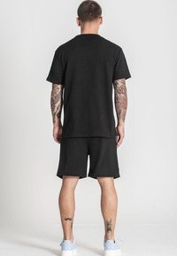 Čierna pletená outfita s tričkom a šortkami. Tričko má voľný strih a krátke rukávy, v kombinácii s ladícími šortkami. Tenisky s modrým vzorom.
