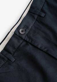 Pantalons bleu marine avec une texture de tissu lisse, fermeture à bouton, coutures surpiquées et une doublure intérieure de couleur claire contrastante.