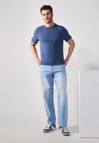 Blå kortermet strikket t-skjorte satt sammen med lysvaskede jeans. Jeansene har avslappet passform, og antrekket er fullført med svarte og hvite joggesko.