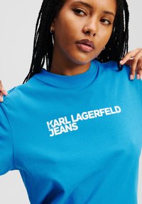 Plava pamučna majica s bijelim logotipom "KARL LAGERFELD JEANS" otisnutim preko grudi; okrugli izrez, kratki rukavi, glatka tekstura.