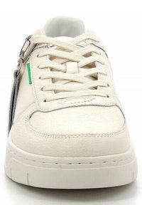 Zapatilla de cuero blanco con puntera redonda, cordones planos y acentos plateados. Presenta una etiqueta verde y una superficie texturizada para un detalle adicional.