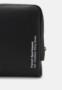 Svart fodral i konstläder med en jämn textur, som har fet vit text som säger "Fransk Sportskläder grundades nitton trettio tre" på sidan.