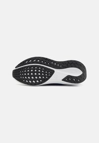 Semelle en caoutchouc noire avec un motif texturé, présentant une semelle intermédiaire blanche et un design lisse et courbé au niveau du talon.