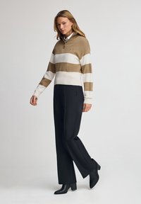 Sudadera de rayas beige y blanca con cuello de media cremallera, combinada con pantalones de pierna ancha negros y botas de tobillo de tacón negras.