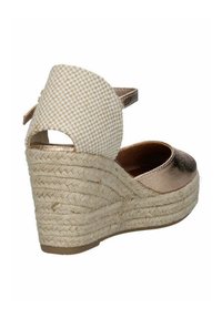 Sandale à talon compensé avec une semelle en jute tressé. Dessus en bronze métallique et bride arrière à carreaux beiges. Design à bout fermé avec bride de cheville.