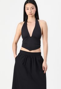 Svart halterneck-top med dyp V-hals og rynket design, kombinert med et høyt midje svart skjørt med elastisk midjebånd og sidelommer.