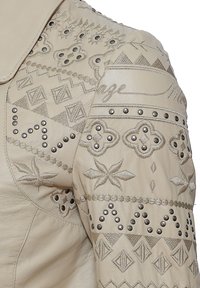 Beige Lederjacke mit aufwendiger Stickerei und Nieten. Verfügt über geometrische Muster und florale Designs, die durch metallische Hardware akzentuiert sind.