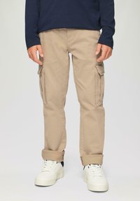 Beige cargo pants with side pockets, slightly rolled cuffs, paired with white sneakers. The fabric appears durable with a smooth texture.