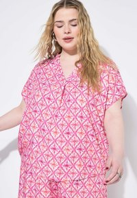 Blusa rosa a fantasia con maniche corte, caratterizzata da disegni a diamante e floreali in diverse tonalità di rosa e bianco. Tessuto leggero.