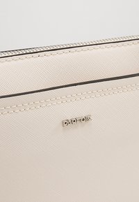 Beige syntetická taštička s texturovaným povrchem, stříbrným zipem a černými detaily. Na přední straně je stříbrné logo "Parfois".