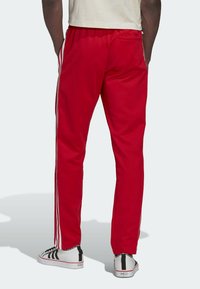 Red athletic pants with white side stripes, made from smooth fabric, featuring an elastic waistband and a back pocket.
