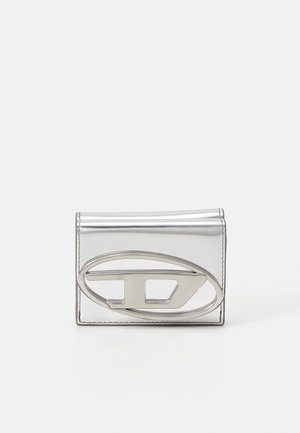 Silver metallic wallet with a smooth texture, featuring a prominent oval-shaped silver hardware accent on the front. Compact rectangular design.