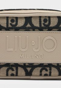 Beige sünteetiline rahakott, millel on must monogrammimuster, reljeefne logo ja sile tekstuur. Ülemise äärte äärde tõmblukk.