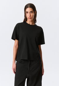 Black cotton t-shirt featuring a round neckline and short sleeves, with a relaxed fit and minimalistic design. No patterns or embellishments.
