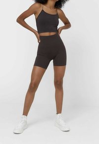 Top corto a coste marrone e pantaloni corti in vita alta abbinati, con un design aderente; modella con sneakers bianche.