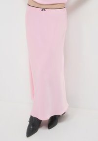 Jupe maxi en satin rose avec une texture lisse, dotée d'une bordure noire à la taille et d'un petit nœud décoratif.