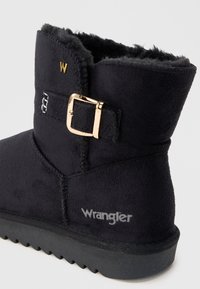 Fekete velúr bokacsizma, puha béléssel, arany fém csattal és szürke Wrangler márkázással az oldalon. Textúrált talp.