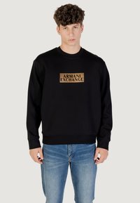Suéter negro con un parche rectangular de logo dorado que incluye el texto "ARMANI EXCHANGE". Fabricado en un tejido suave con puños y dobladillo acanalados.