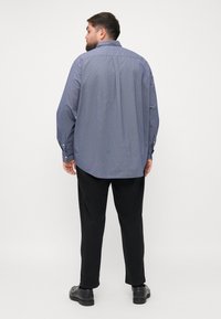 Męska koszula z długim rękawem w kolorze niebieskim z geometrycznym wzorem, z kołnierzykiem zapinanym na guziki i regulowanymi mankietami, w połączeniu z czarnymi spodniami.