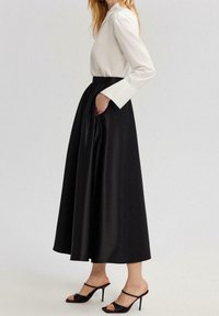 Falda de satén negra con cintura elástica y bolsillos, combinada con una blusa blanca de manga larga y sandalias de tacón negras.