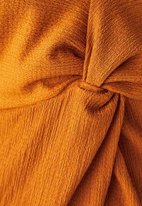 Texturerad tyg i en rik orange nyans, med en knuten accent. Ytan visar ett ribbat mönster som skapar djup och visuell intresse.