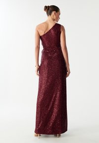 Celosrstý vínový večerní šat s jedním ramenem, zdobený flitry, s přiléhavým pasem a splývavou sukní, bez viditelných ozdob.