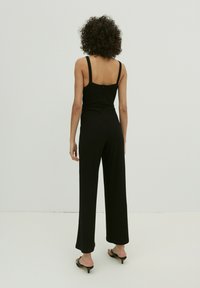 Schwarzer, gerippter Jumpsuit mit weiter Beinform und verstellbaren Spaghetti-Trägern. Er bietet ein tailliertes Oberteil und einen Reißverschluss auf der Rückseite.